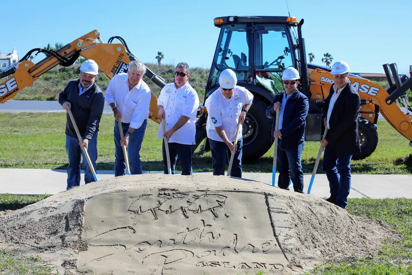 Patrick McNulty and City officials in hard hats breaking ground on a South Padre Island project, with a backhoe behind them.